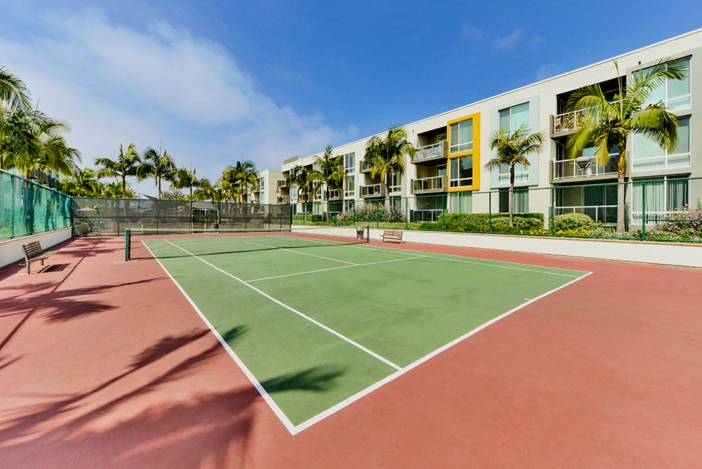 a tennis court in front of a building with palm trees