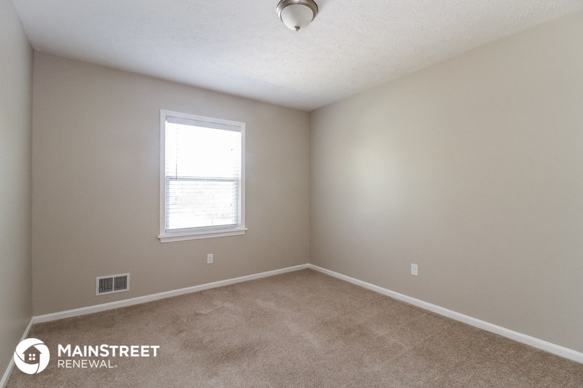 the spacious bedroom with carpeted flooring and a window