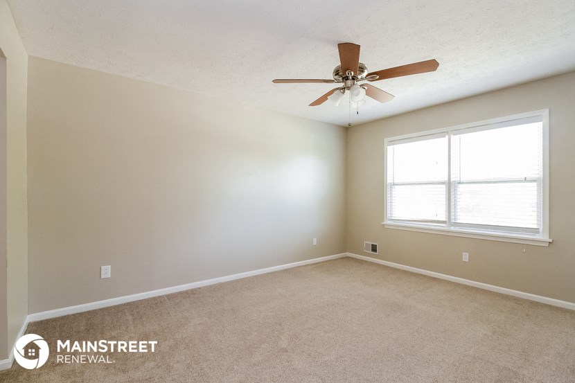the spacious living room with ceiling fan and window