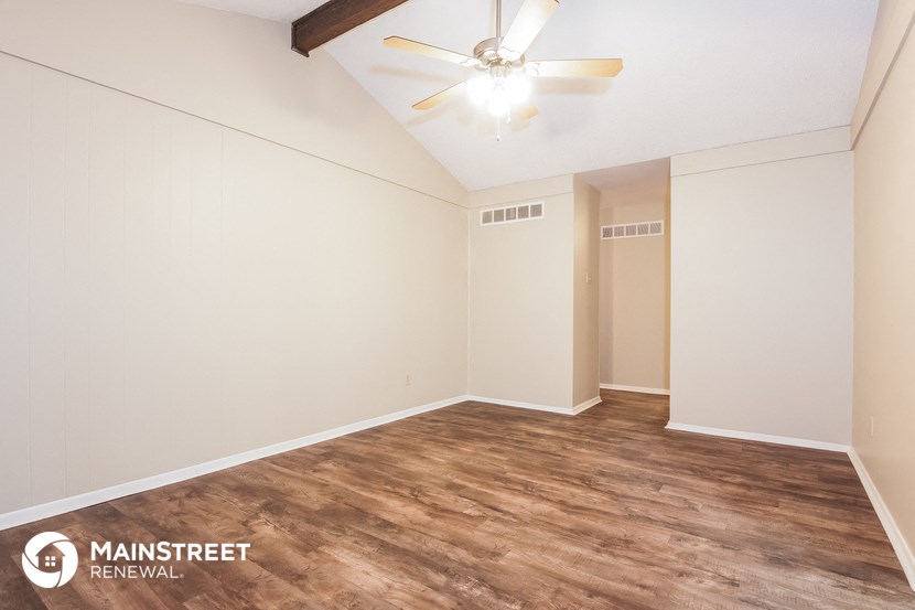 the spacious living room with wood flooring and a ceiling fan