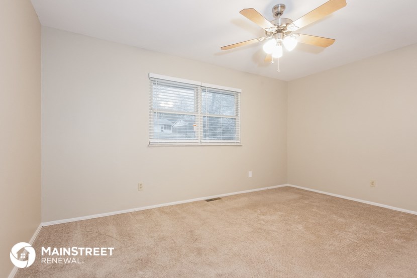 the spacious living room with ceiling fan and carpeting