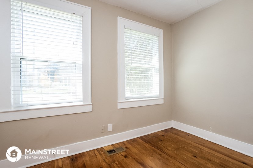 the living room of a home with two windows and a wooden floor
