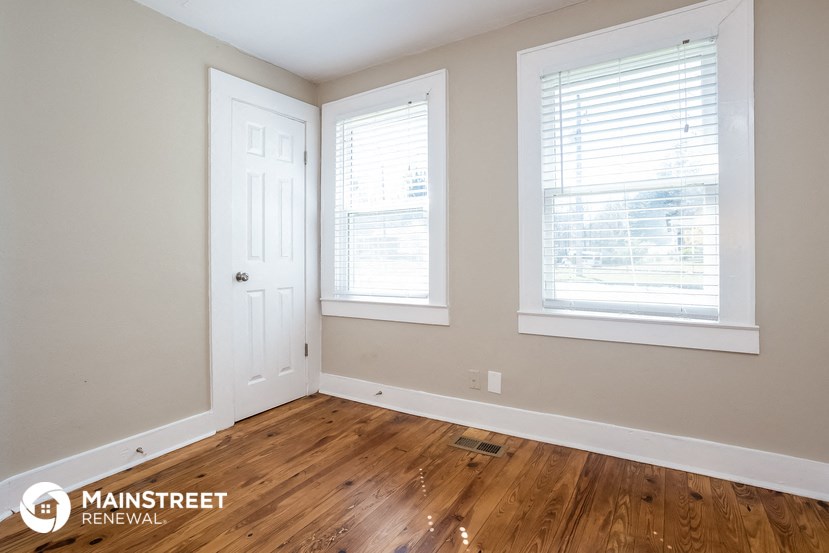 a bedroom with wood floors and a door and two windows