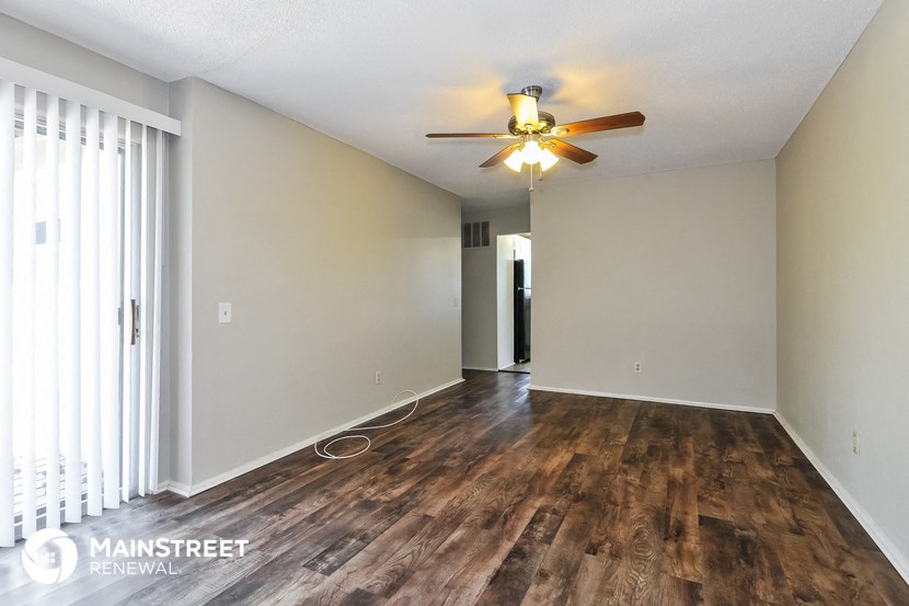 the living room and dining room of an apartment with wood floors and a ceiling fan