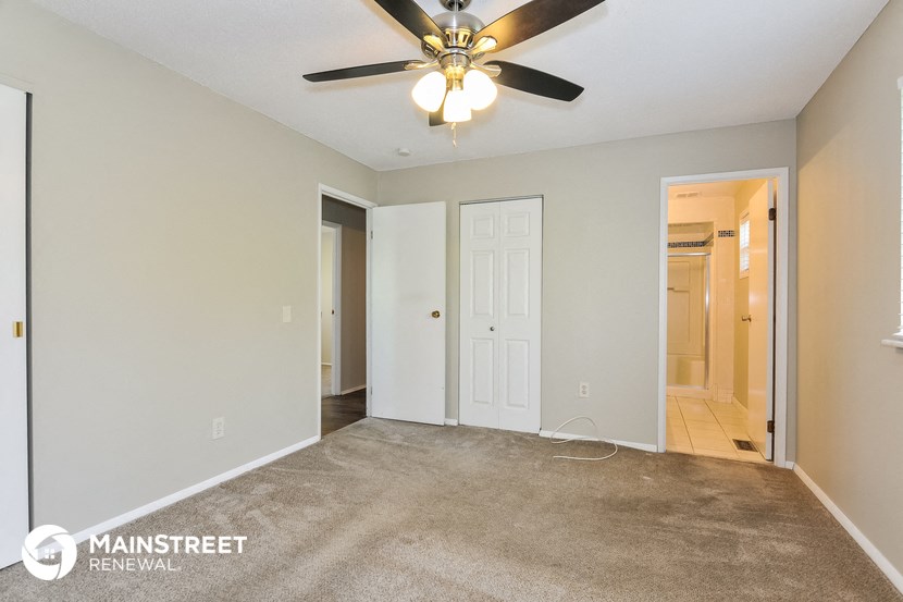 the living room of an apartment with carpet and a ceiling fan