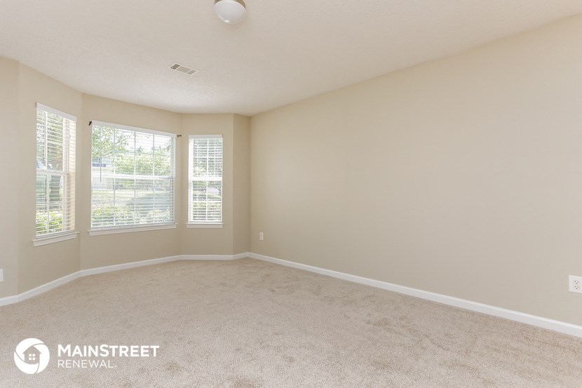 the spacious living room of this manufactured home has carpeting and windows