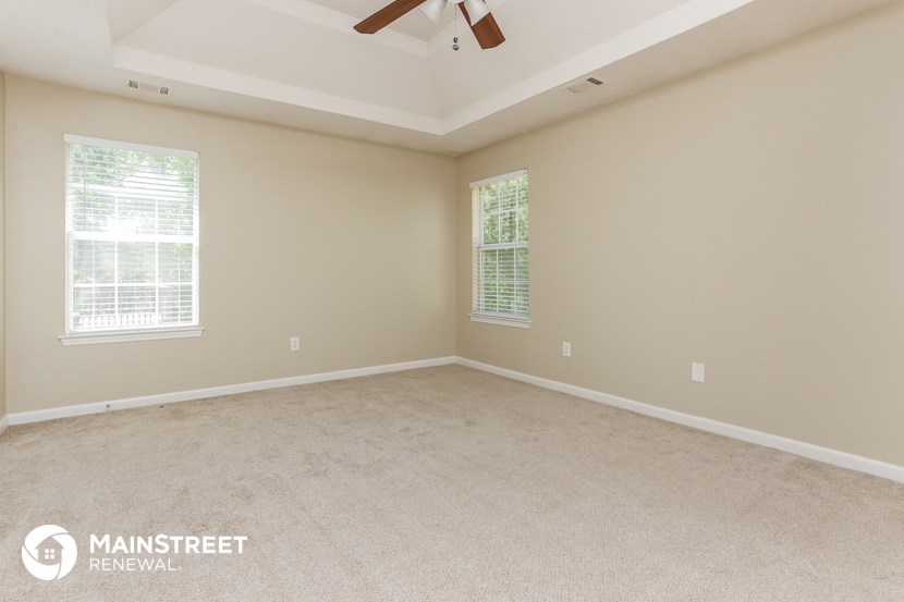 an empty living room with a ceiling fan and two windows
