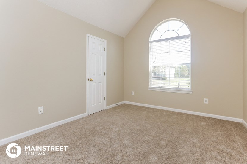 a bedroom with carpet and a white door and a window