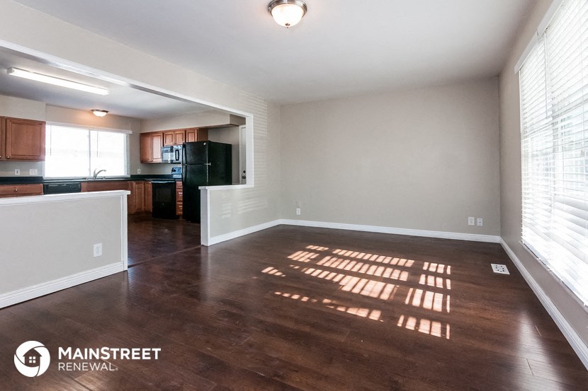 an empty living room with wood flooring and a kitchen
