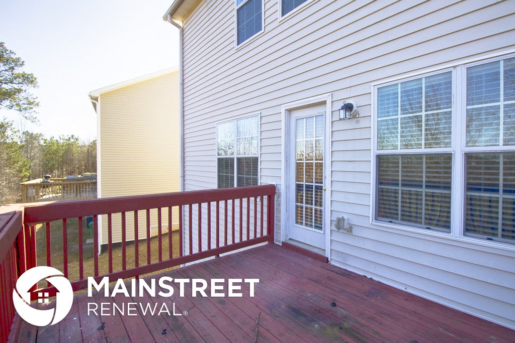 a deck in front of a white house with a red railing