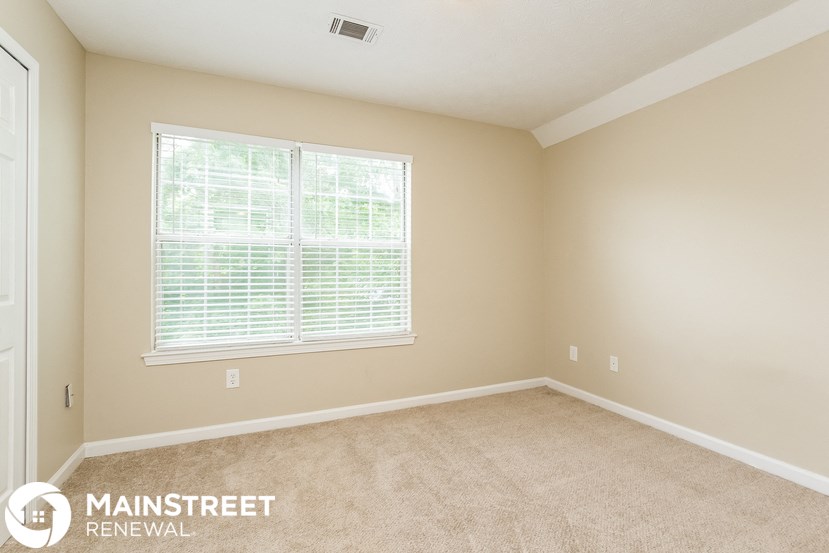a bedroom with a large window and beige carpet