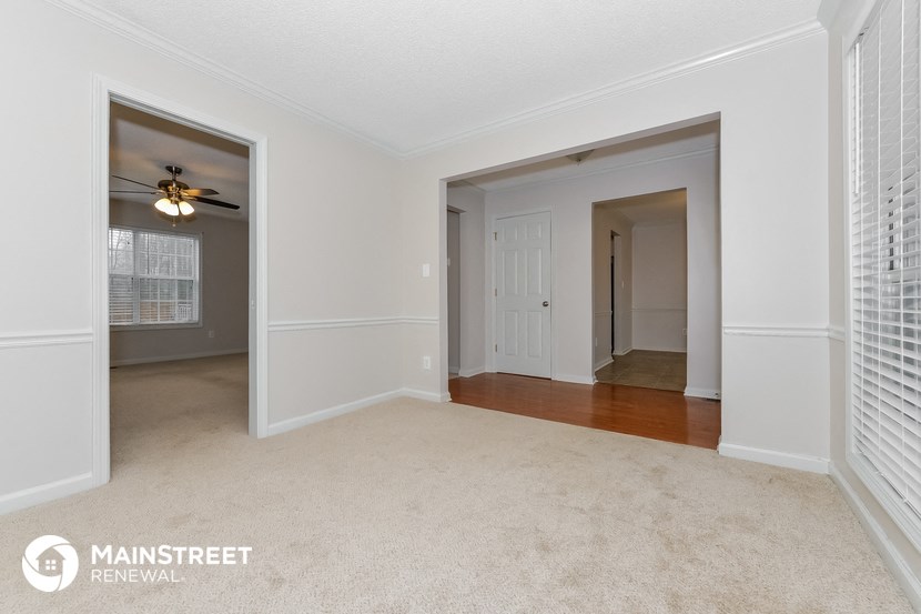 an empty living room with a ceiling fan and a door to a hallway