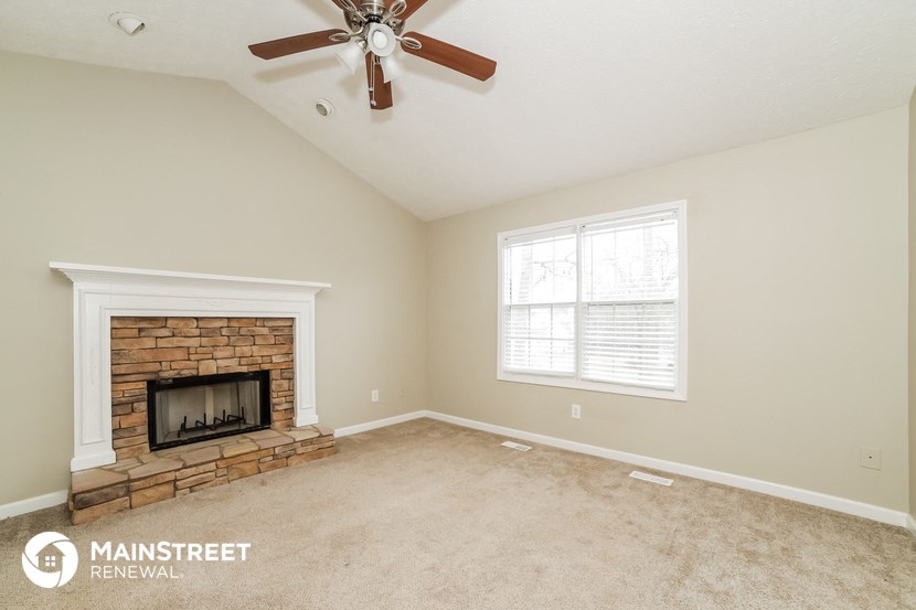 a living room with a brick fireplace and a ceiling fan