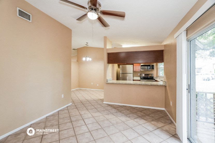 an empty living room with a ceiling fan and a kitchen
