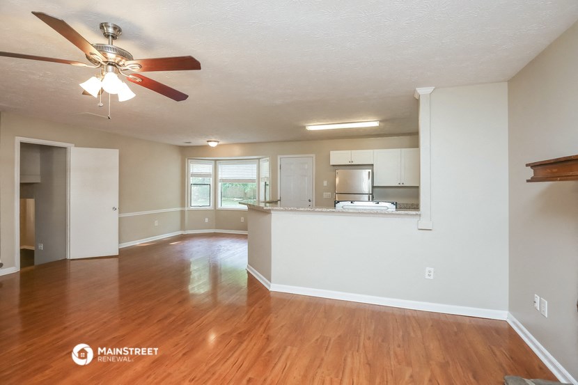 an empty living room with a kitchen and a ceiling fan
