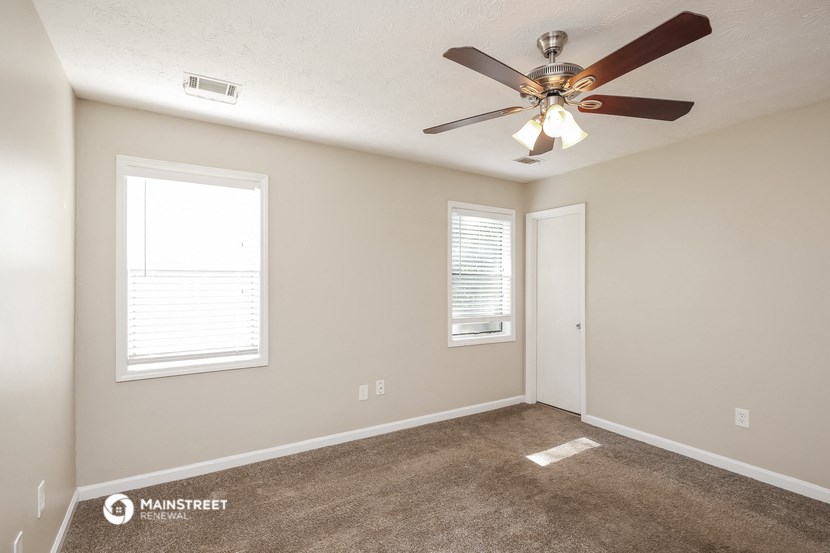 an empty room with a ceiling fan and two windows