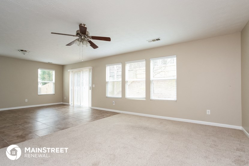 an empty living room with a ceiling fan and windows