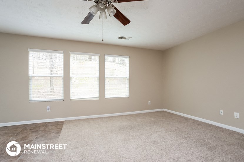 an empty living room with a ceiling fan and three windows