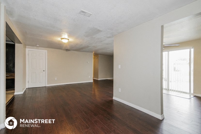the living room and dining room of an apartment with wood flooring and white walls