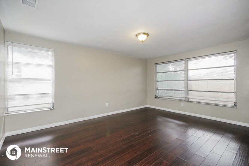 the living room of an apartment with wood flooring and two windows