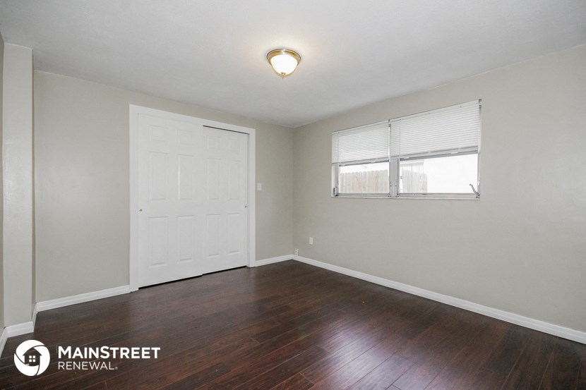 the living room of a small rental house with wood flooring and a window