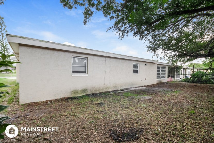 the side of a white house with a yard and trees