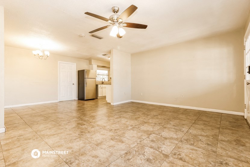 an empty living room with a ceiling fan and a kitchen