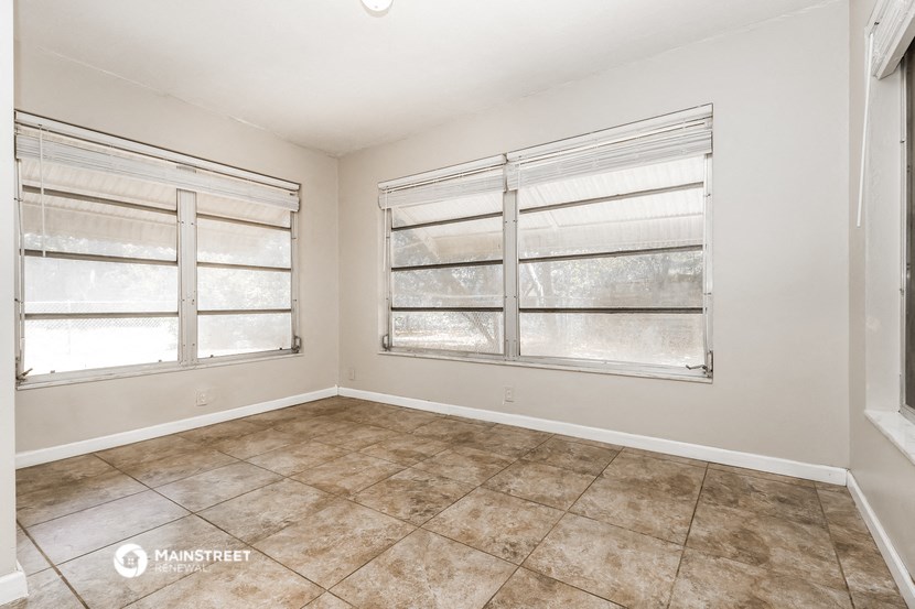 an empty living room with three windows and a tiled floor