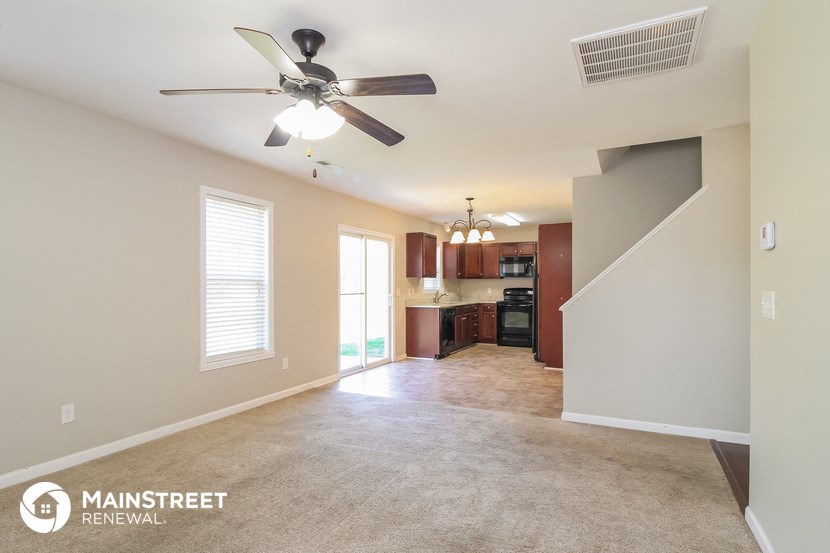 an empty living room with a ceiling fan and a kitchen