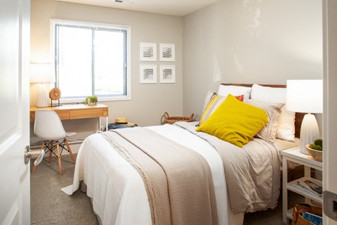 A bedroom with a bed, desk, chair, and window.