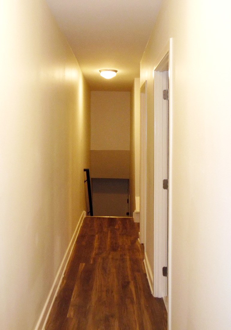 a hallway with wood floors and white walls and a chair
