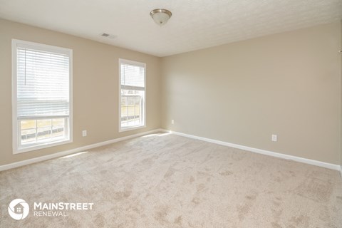 a spacious living room with carpet and two windows