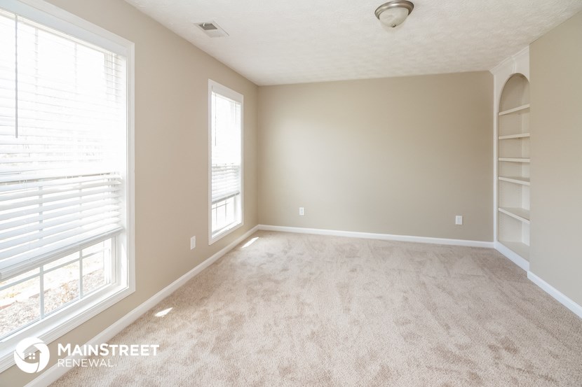 an empty living room with white carpet and two windows