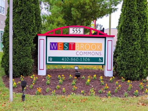 a sign for west brook commons on a lawn with flowers