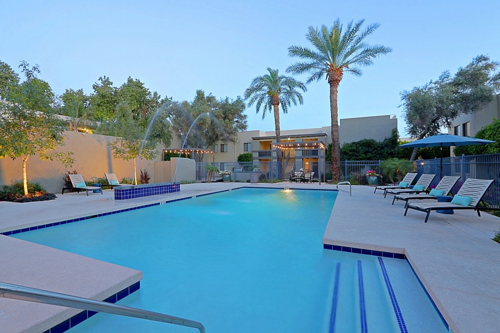 a large swimming pool with chairs and palm trees
