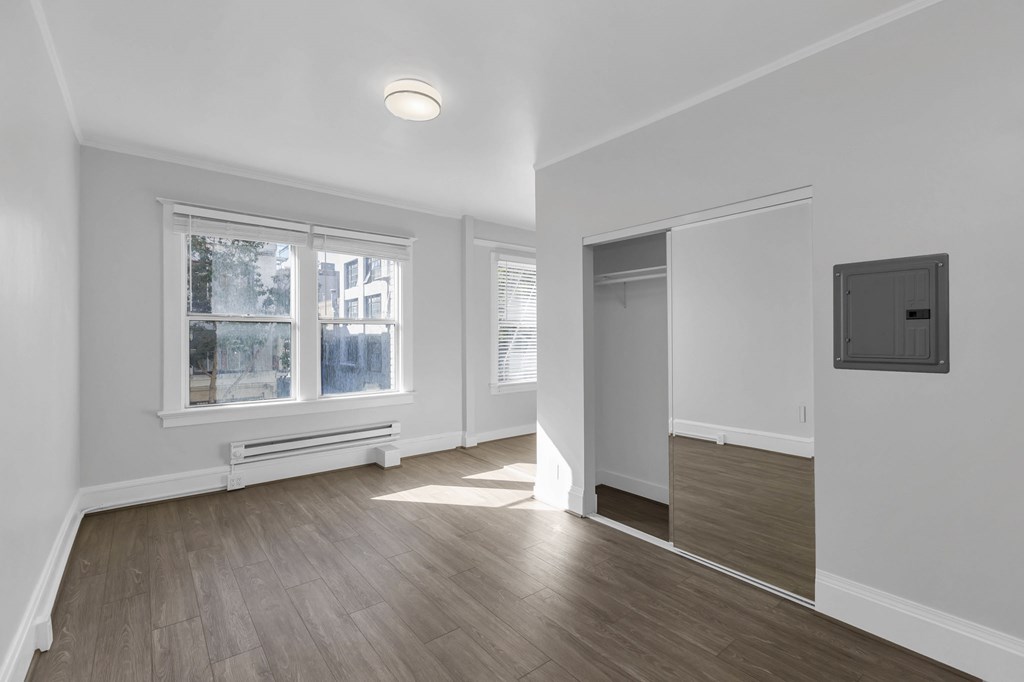 a living room with white walls and wood flooring and a door to a hallway