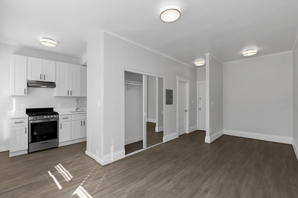 a renovated living room with white walls and a kitchen with white cabinets and black appliances