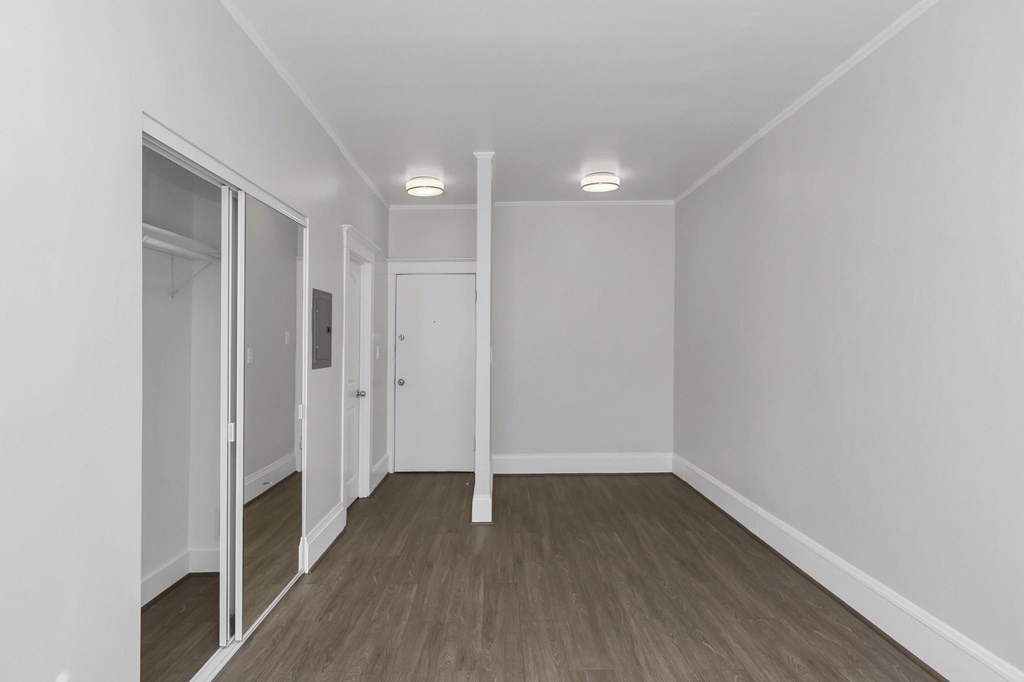a living room with white walls and wood floors and a mirrored closet