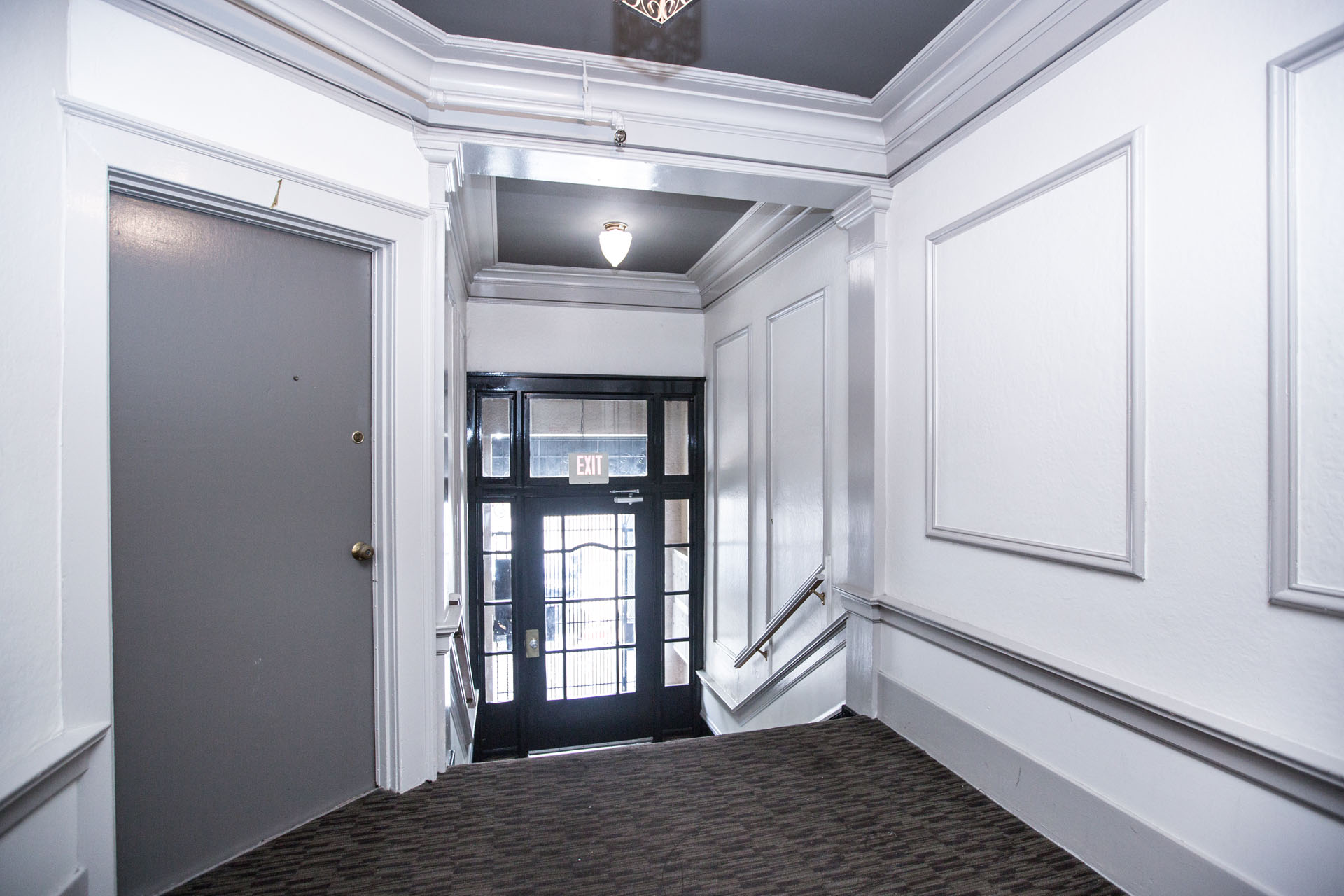 A hallway with a black door and a white wall.