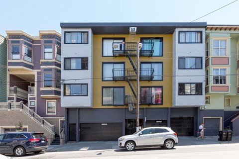 A row of modern apartment buildings with cars parked in front.