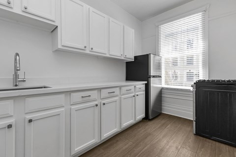 A black refrigerator is in a kitchen with white cabinets.
