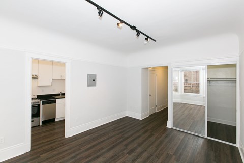 A room with a kitchen area in the background and a sliding glass door leading to a balcony.