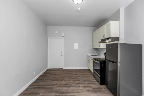 A kitchen with a black refrigerator and wooden floors.