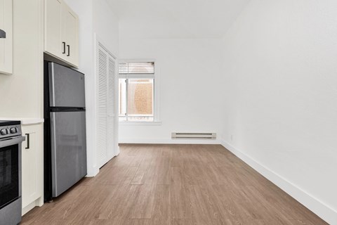 A kitchen with a black fridge and stove, a window with blinds, and a wooden floor.