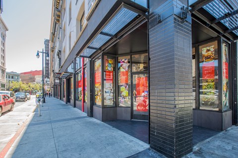A street view of a building with a red car parked on the side of the road.