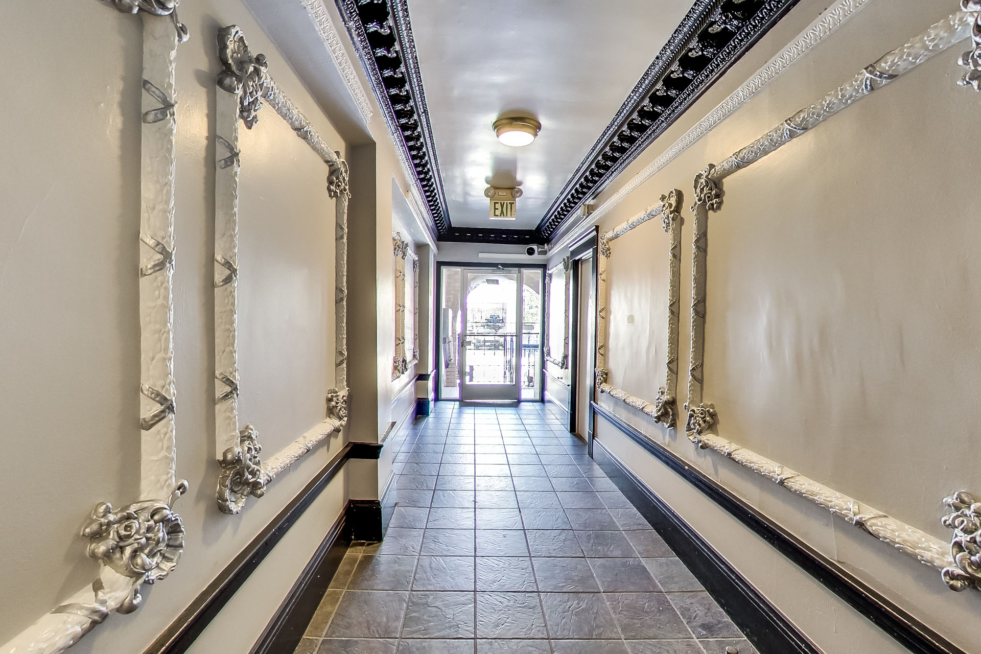 A long hallway with a black tile floor and white walls with gold trim.
