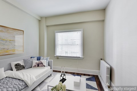 A bedroom with a bed, pillows, a nightstand, a window with blinds, a painting on the wall, a rug on the floor, and a vase with flowers on the nightstand.