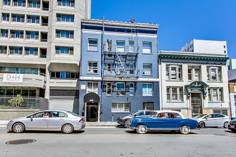 A blue car is parked in front of a blue building with a fire escape.