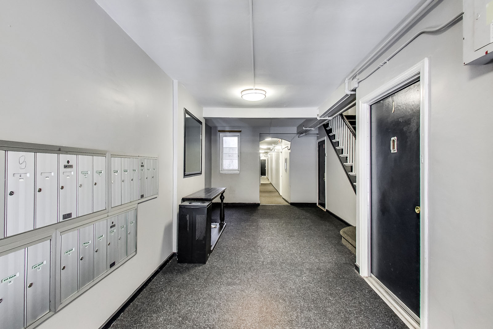 A long hallway with a black door on the right and a staircase on the left.