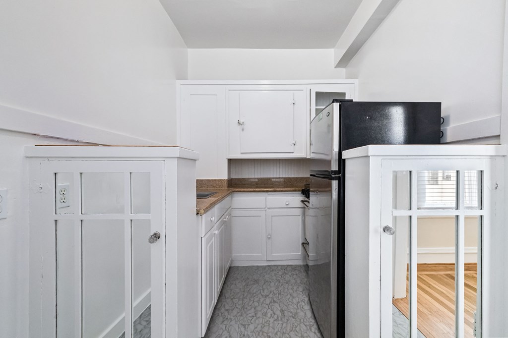 A kitchen with white cabinets and a black fridge.